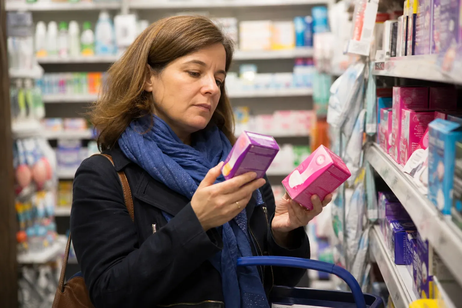 Une femme compare deux boîtes de produits d'hygiène intime dans une pharmacie et lit attentivement les étiquettes